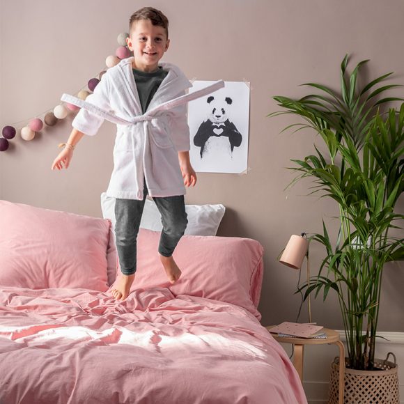 Un garçon en peignoir sur un lit rose